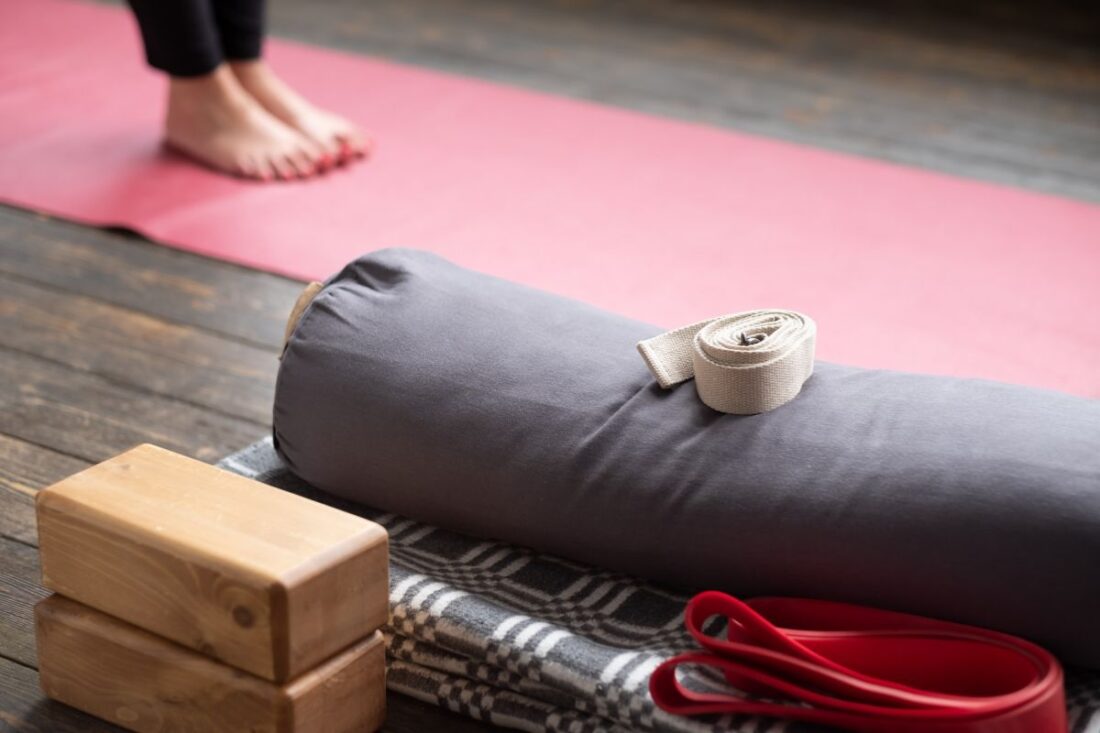 Selección de accesorios de yoga: bolster, bloques, manta y cinturón sobre esterilla
