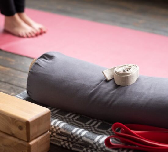 Selección de accesorios de yoga: bolster, bloques, manta y cinturón sobre esterilla