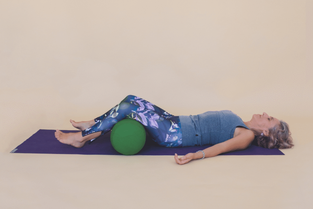 Persona en Savasana con las rodillas sostenidas por un bolster al final de su práctica de Yin yoga