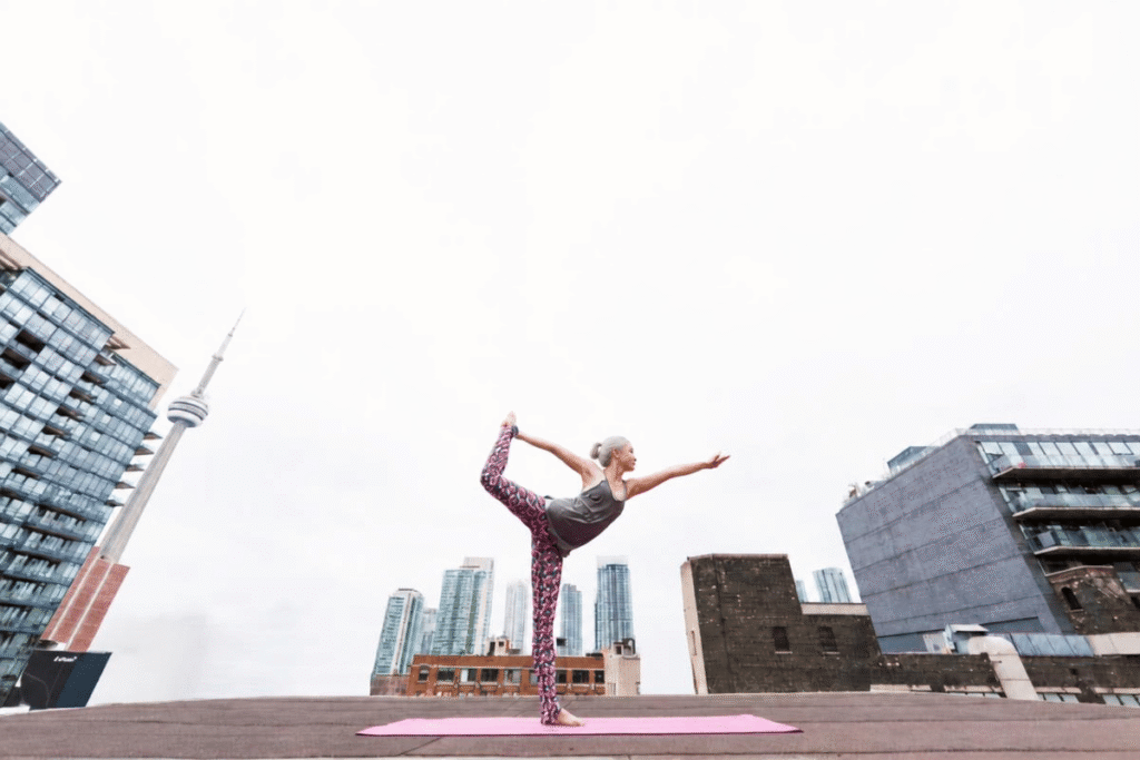 Mujer practicando yoga sobre una esterilla en una azotea con vistas al perfil de la ciudad